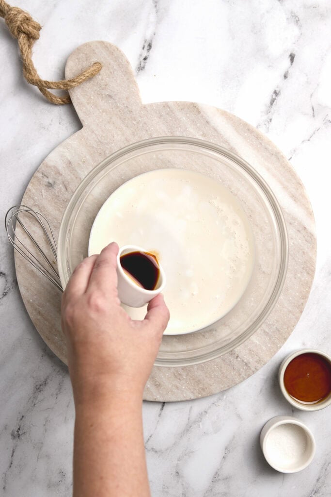 Homemade vanilla frosting mixture with vanilla and other ingredients in glass bowl.