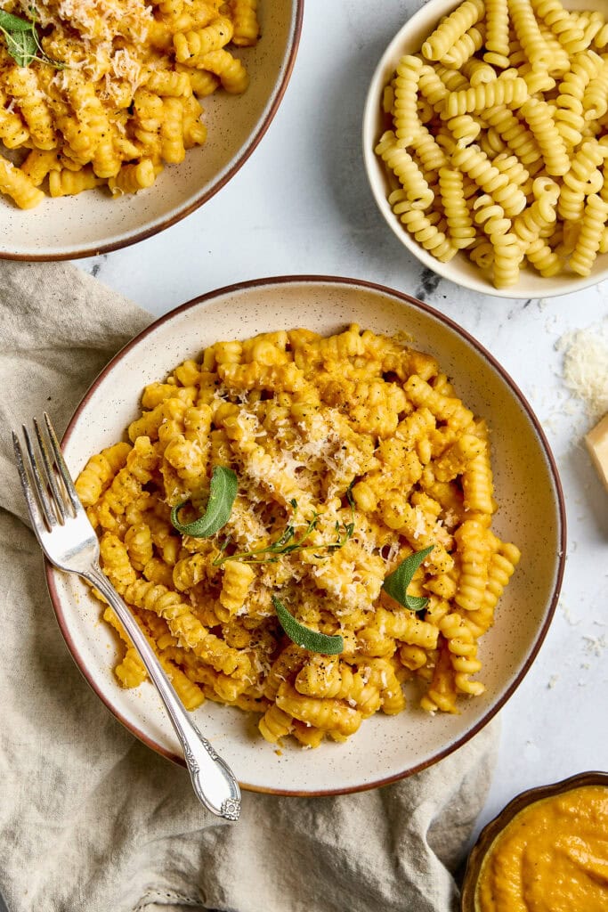 Creamy butternut squash pasta with sage and parmesan cheese, served in rustic bowls, on light background, with additional ingredients, cozy and inviting, perfect comfort food recipe, delicious vegetarian meal.