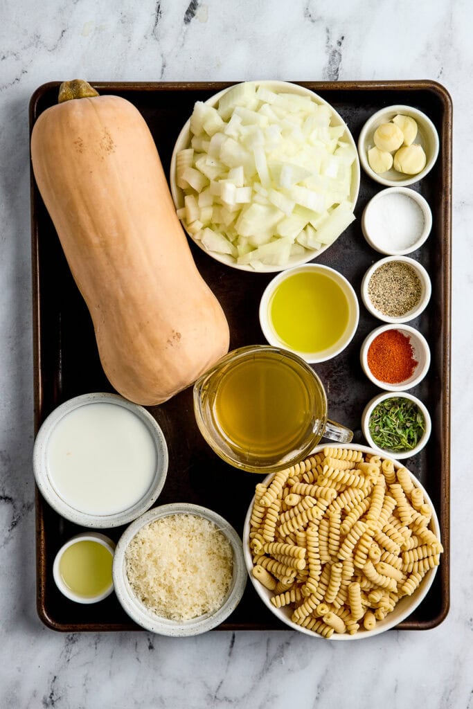 Creamy butternut squash pasta sauce ingredients with pasta, onions, garlic, and spices on a tray.