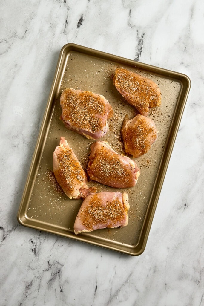 Juicy curry chicken thighs seasoned with spices and herbs on a baking sheet ready for roasting.