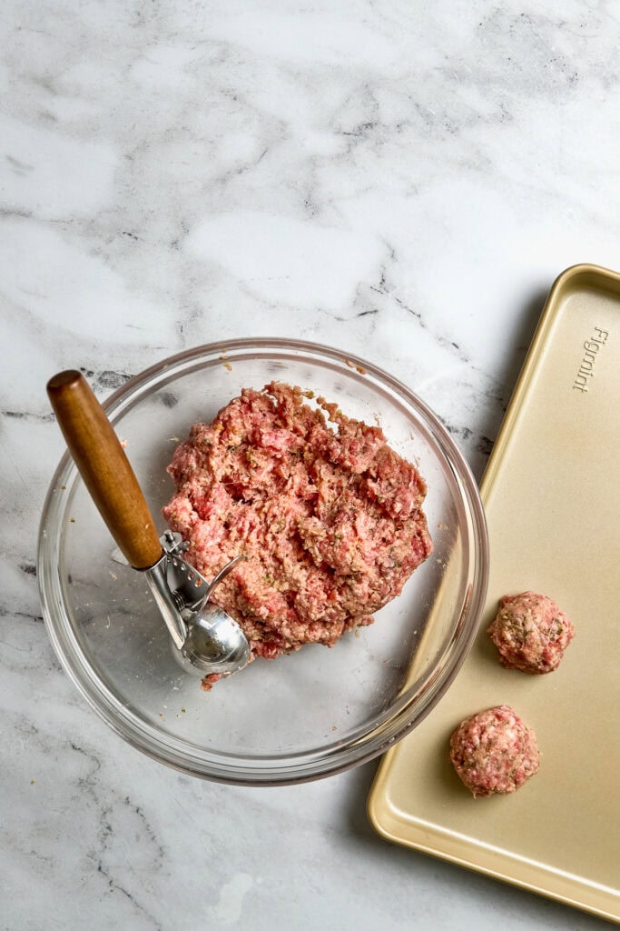 Cream cheese mixture for homemade meatballs in a glass bowl on marble surface with meatball ingredients ready to shape and bake.