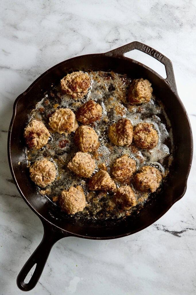 Crispy homemade meatballs frying in cast iron skillet with bubbling oil, ready to be served, popular comfort food, delicious savory dish, perfect for family dinner or appetizer.