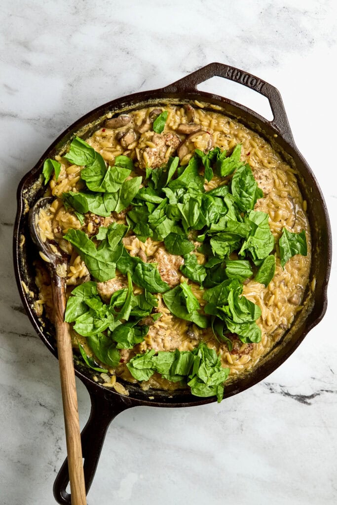 Creamy mushroom and spinach pasta dish in a cast iron skillet, topped with fresh spinach leaves, served on a marble surface. Delicious, hearty, and perfect for dinner or special occasions.