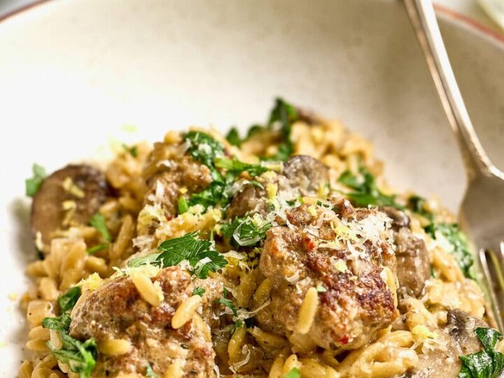 Creamy mushroom orzo pasta dish with spinach and meatballs and cheese in a white bowl.