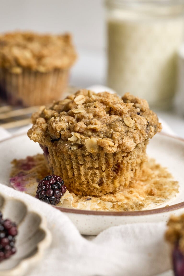 Delicious homemade blackberry oatmeal muffin topped with oats and crumbly streusel, perfect for breakfast or snack. Fresh blackberries and a cozy bakery vibe highlight this bakery-style muffin.