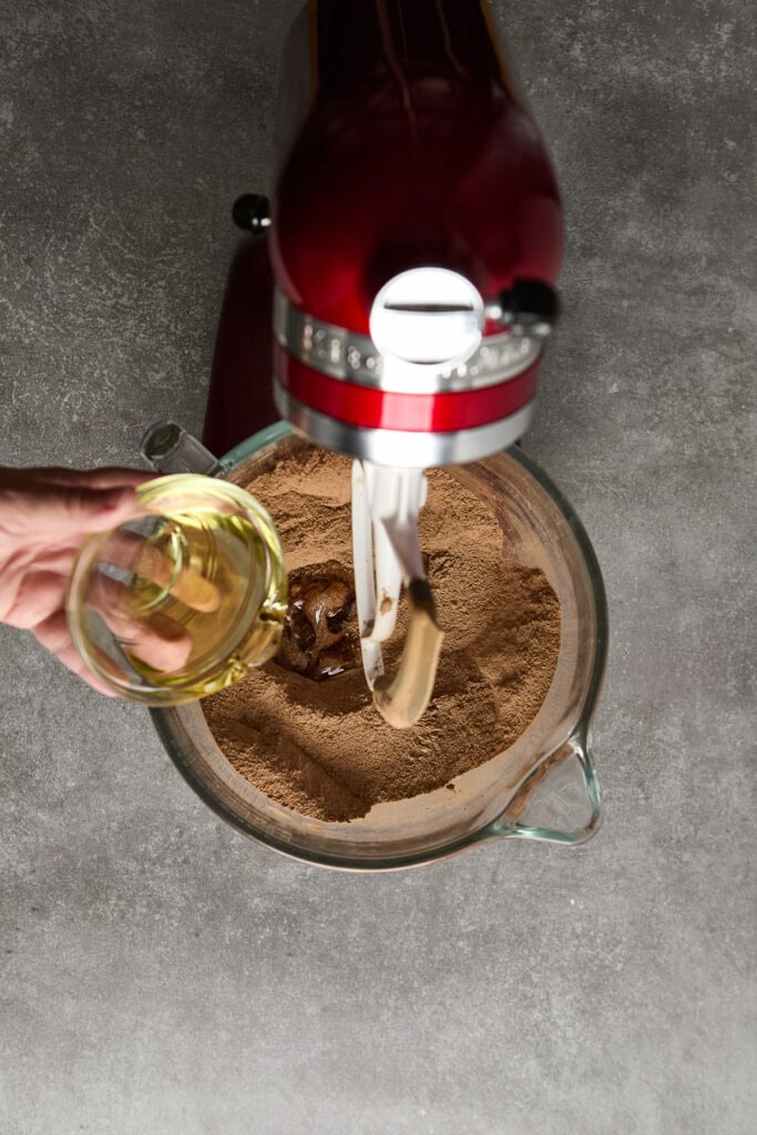 Rich chocolate cake batter being mixed with a stand mixer in a glass bowl.