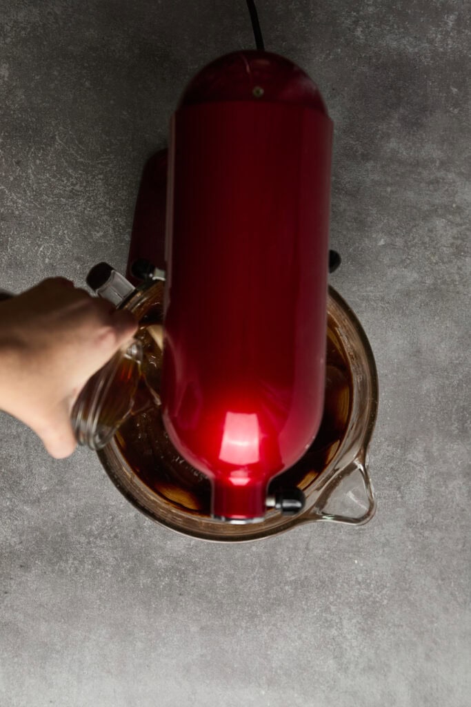 Narrow-neck glass infusion bottle with a red silicone lid, used for making flavored iced tea with fresh ingredients and herbs. Perfect for tea lovers, stylish, and reusable.