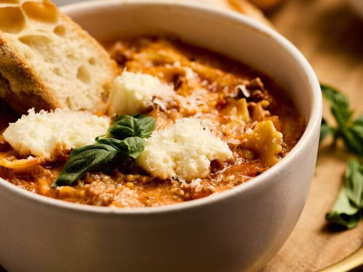 Delicious lasagna soup with ground beef garnished with melted cheese and herbs, served with toasted garlic bread for a comforting meal.