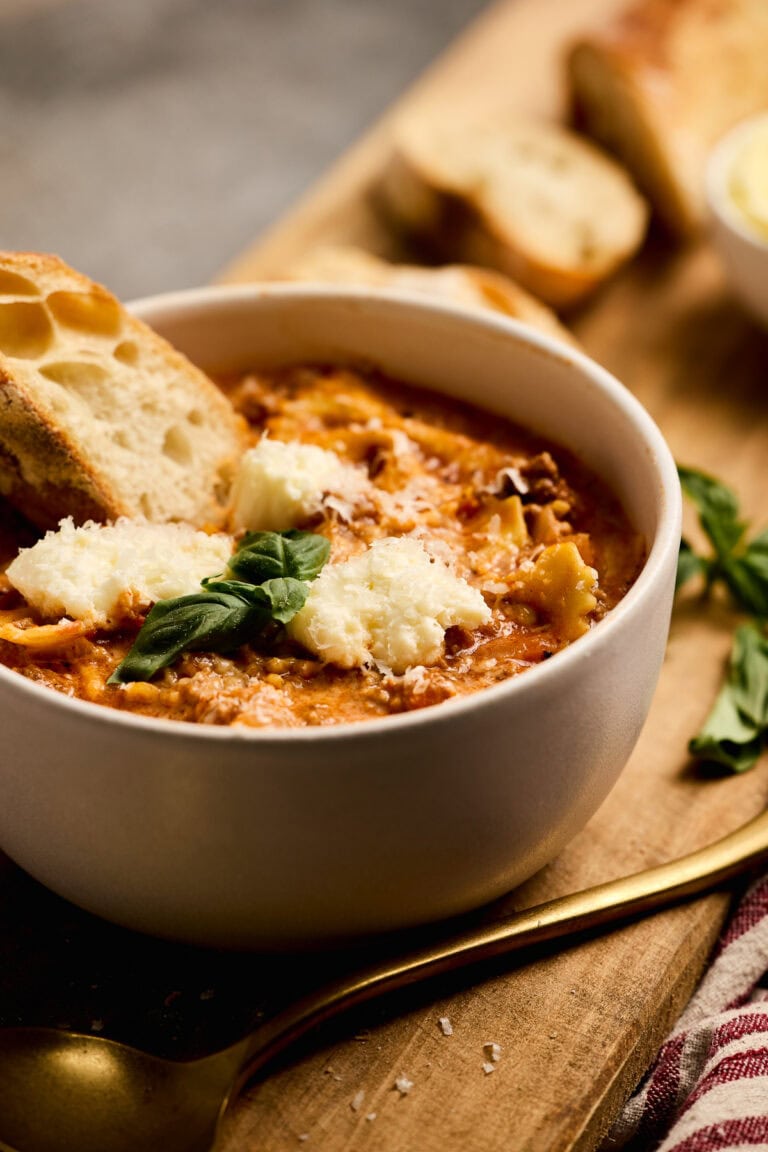 Delicious lasagna soup with ground beef garnished with melted cheese and herbs, served with toasted garlic bread for a comforting meal.