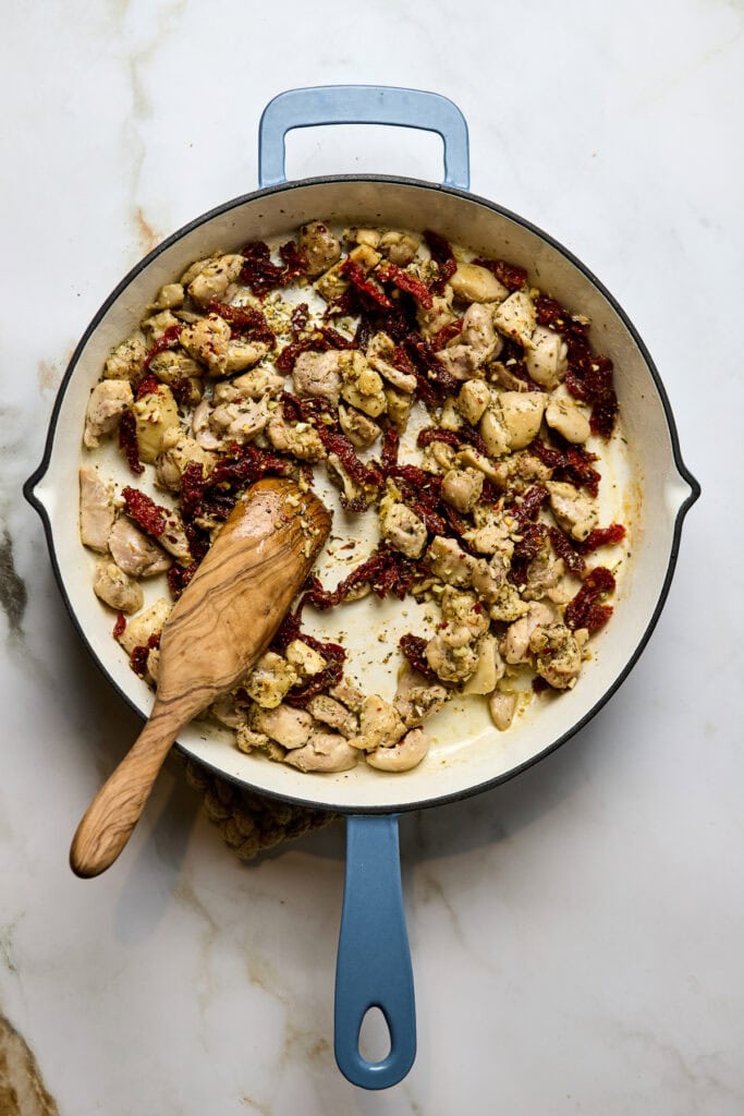 Juicy chicken pieces cooked with sun-dried tomatoes in a flavorful creamy sauce, prepared in a blue cast iron skillet. Perfect for a delicious dinner recipe with herbs and a savory taste.