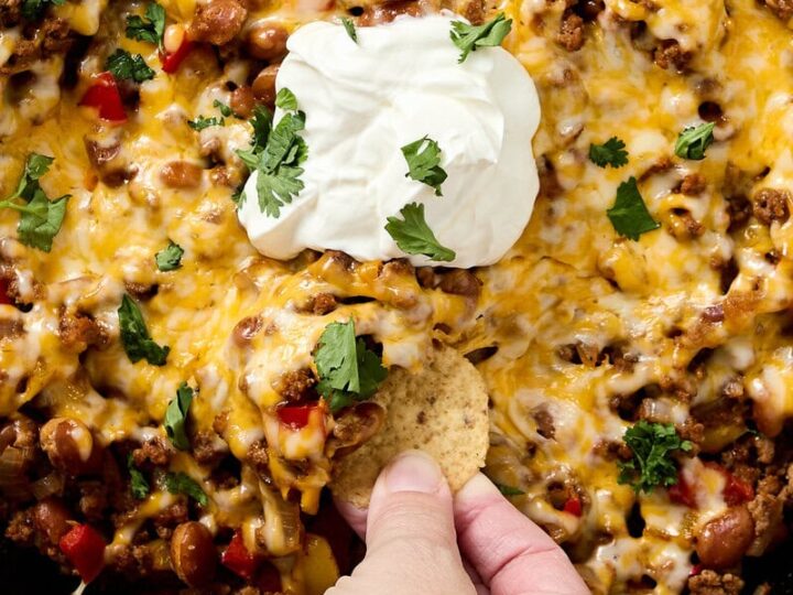 Delicious beef taco skillet with melted cheese, ground beef, beans, and vibrant red peppers, garnished with fresh cilantro and a dollop of sour cream, served with crunchy tortilla chips.