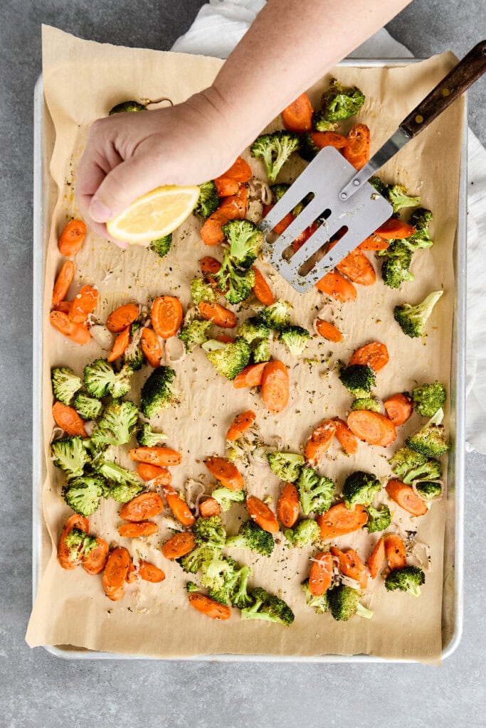 Roasted broccoli and carrots on a baking sheet with parchment paper, prepared for oven roasting.