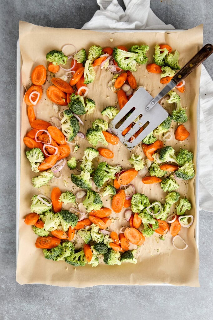 Baked broccoli, carrots, and onions on parchment paper with a spatula, ready for roasting or serving.