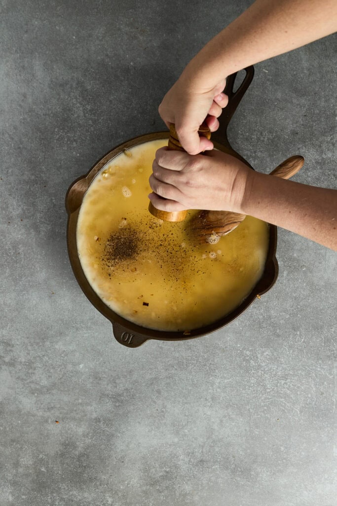 Hands squeezing fresh lemon into a skillet with melted butter, creating a flavorful lemon butter sauce for cooking or dipping.