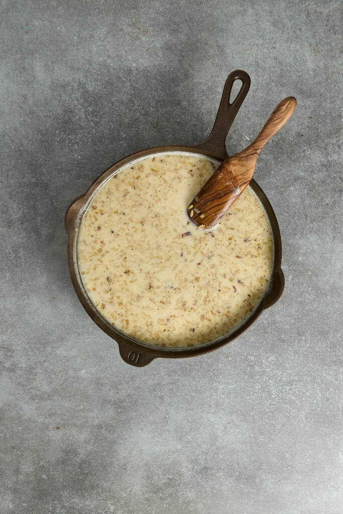 Creamy cheese sauce in a cast iron skillet with a wooden spoon, perfect for dipping or drizzling over dishes. Ideal for comfort food recipes, cheese lovers, and homemade cooking enthusiasts.