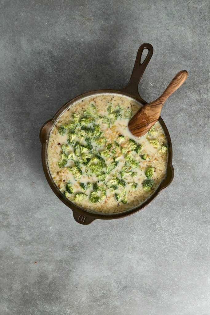 Creamy broccoli cheese skillet with fresh broccoli florets and melted cheese, served in a cast iron pan with a wooden spoon, perfect for comfort food lovers.