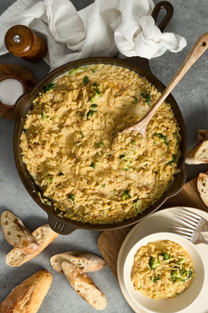 Hearty chicken and rice soup in a black skillet with fresh herbs, served with bread slices and a bowl of soup, perfect for comfort food.