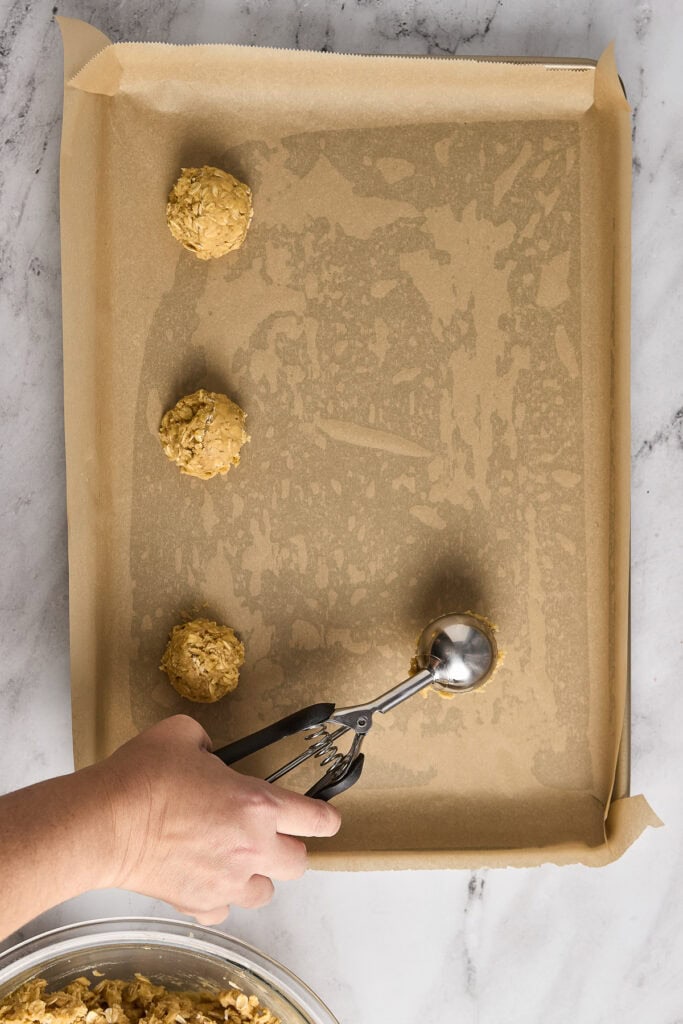 Delicious soft and chewy oatmeal cookies made with rich brown butter, perfect for satisfying sweet cravings. Freshly baked cookies displayed on a baking sheet with a hand using tongs.