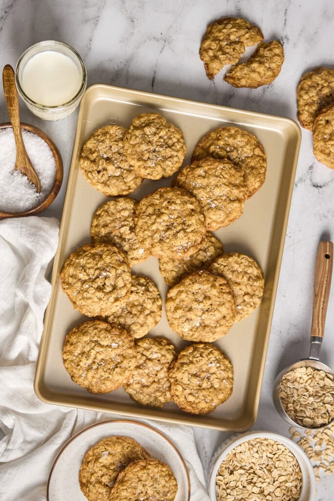 Delicious soft and chewy brown butter oatmeal cookies on a baking tray, with ingredients like oats, milk, and sugar visible around. Perfect for cookie lovers.