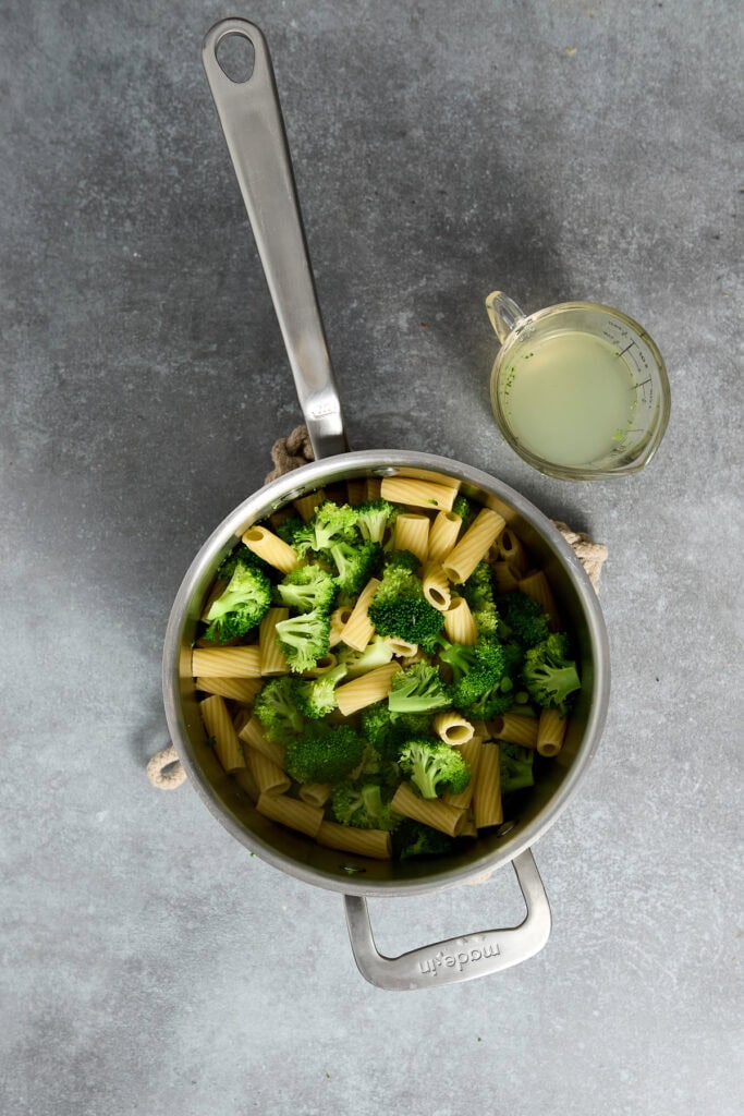 Top view of a skillet with cooked pasta, broccoli, and melted cheese, served with a lemon sauce in a small glass pitcher, perfect for a Chicken Parmesan skillet dish.