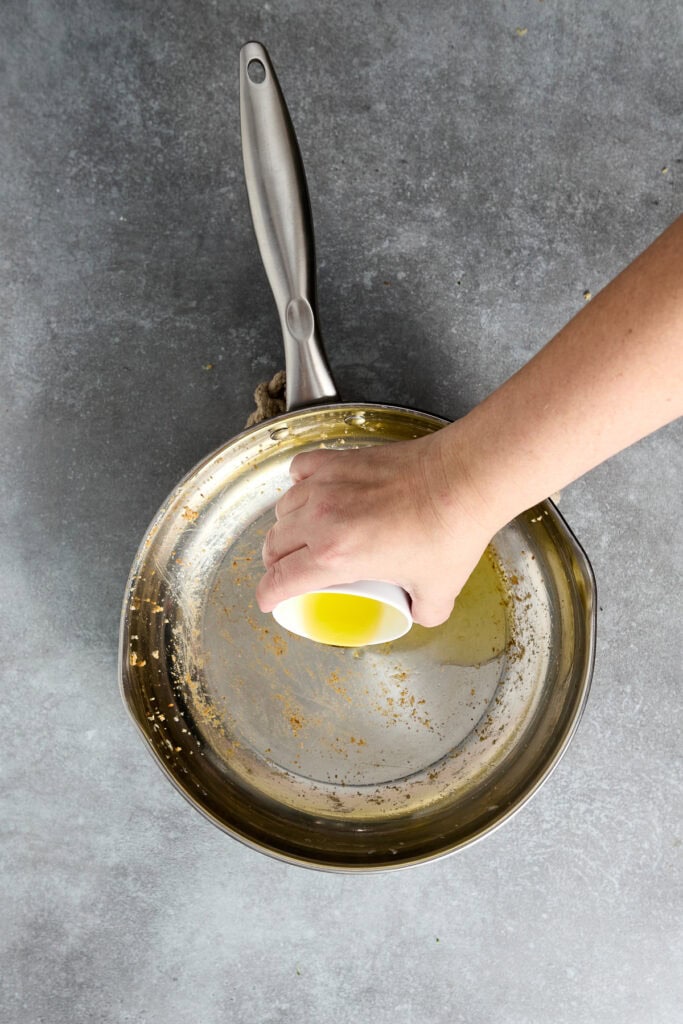 Hand pouring olive oil into a skillet for Chicken Parmesan, showcasing a cooking process for a delicious Italian-inspired dish.