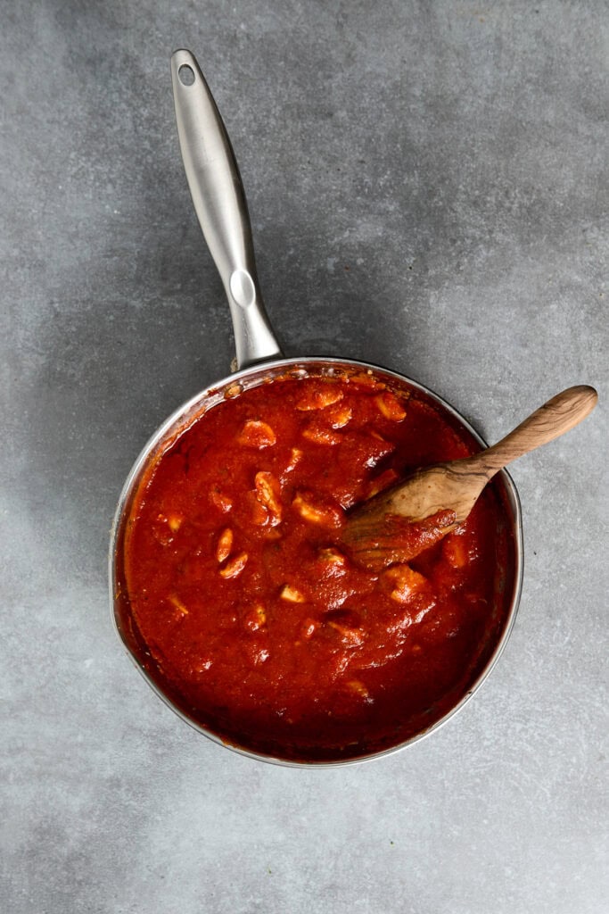 Close-up of a skillet filled with rich, homemade chicken Parmesan sauce with melted cheese and tomato chunks, ready to serve.