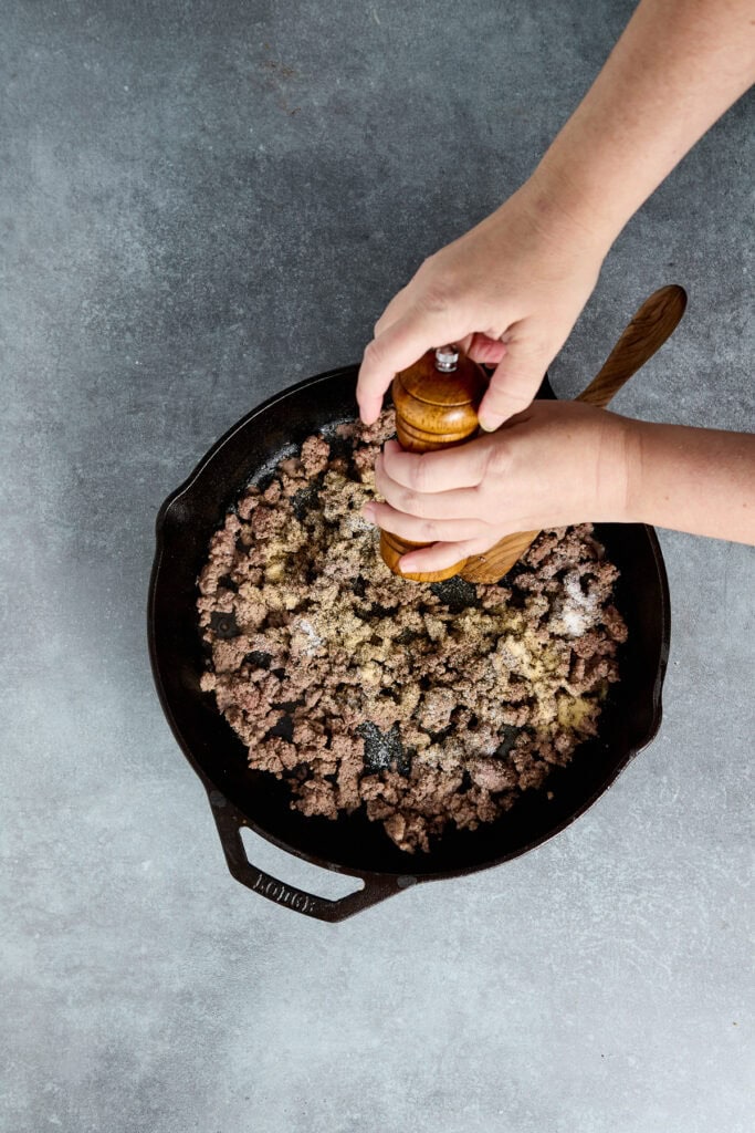 Ground meat being seasoned in a cast iron skillet for cooking or recipe preparation.