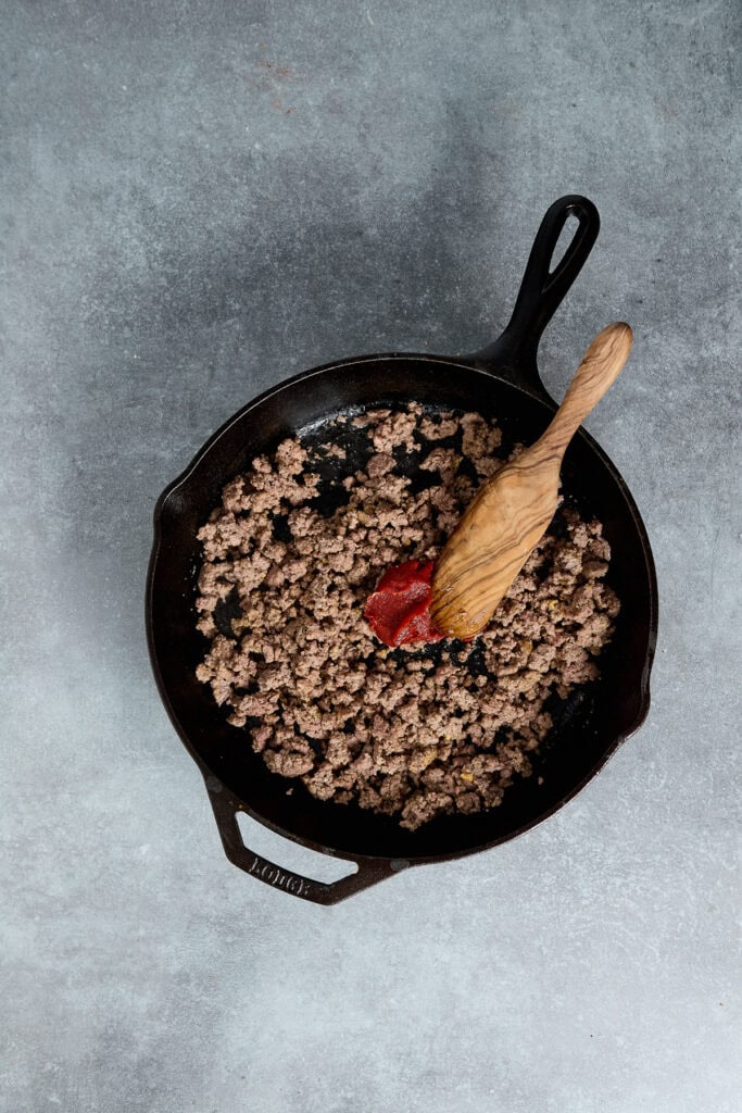 Cooked ground beef in a cast iron skillet with a wooden spoon, ready to serve as a hearty breakfast or dinner dish.