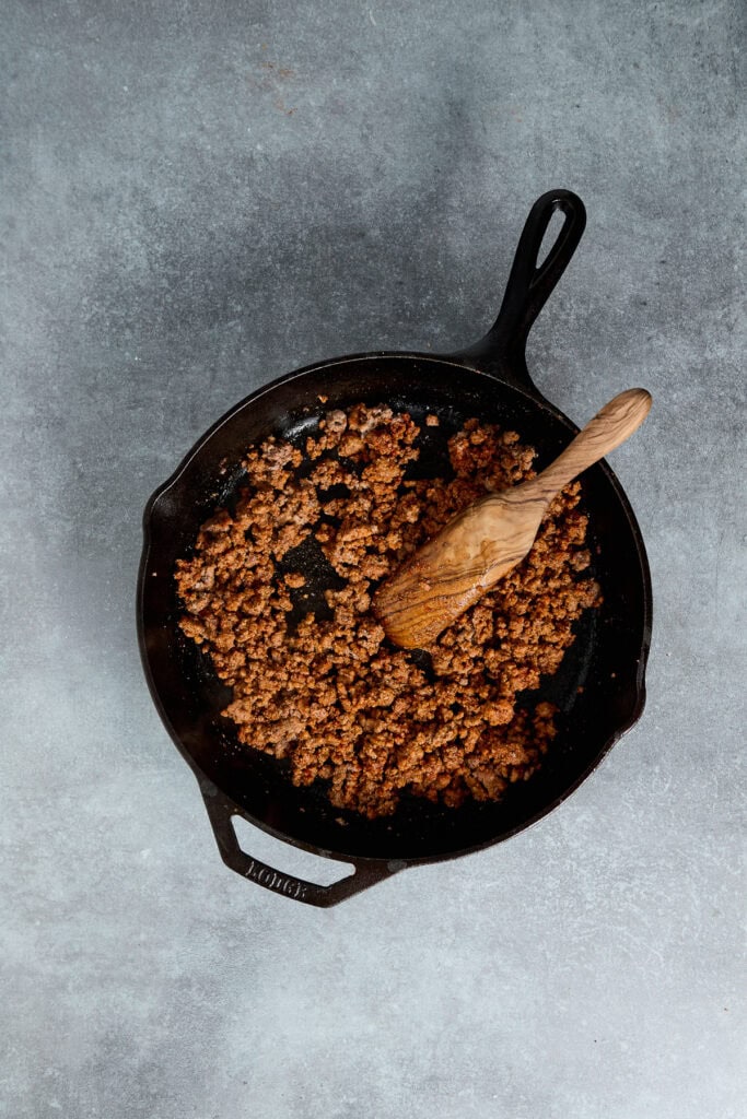 Ground beef cooking in a cast iron skillet with a wooden spoon, perfect for meal prep or recipes.