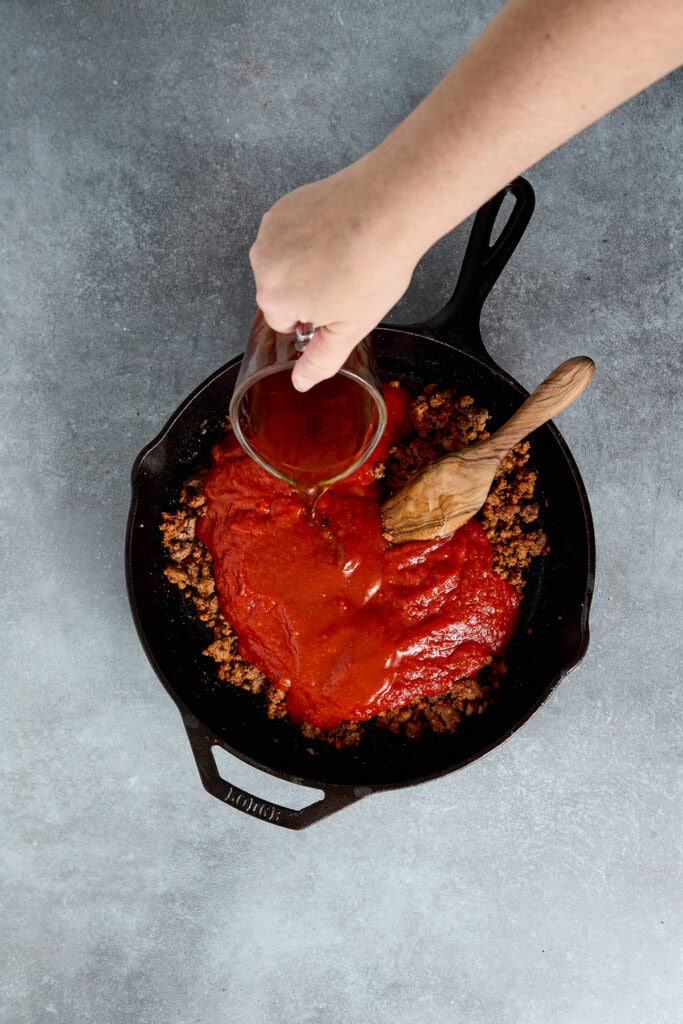 Cooking sweet and sour meat sauce in a skillet with ground meat, tomato sauce, and spices, ready to serve as a flavorful dish.