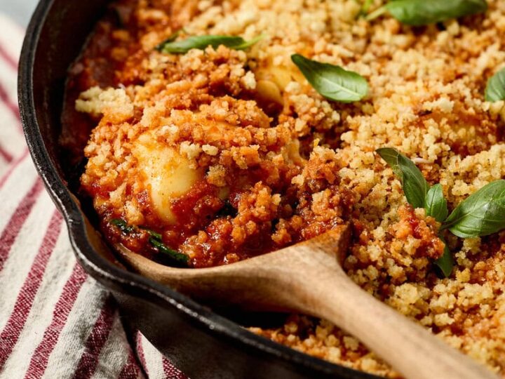 Delicious ground beef and spinach ravioli with tomato sauce, golden breadcrumb topping, and fresh basil garnishes in a black skillet. Perfect comfort food for family dinners.