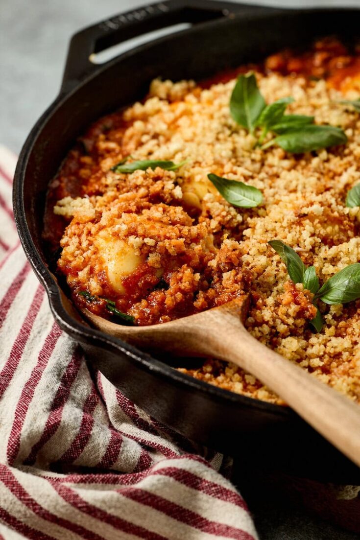Delicious ground beef and spinach ravioli with tomato sauce, golden breadcrumb topping, and fresh basil garnishes in a black skillet. Perfect comfort food for family dinners.