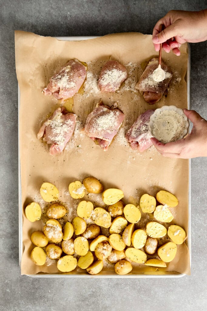 sprinkling seasoning on ranch chicken thighs with sliced potatoes