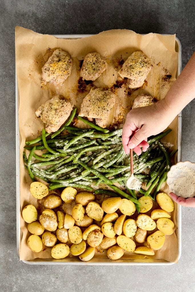 Freshly baked ranch chicken thighs and vegetable roast with green beans, baby potatoes, and seasoned chicken pieces on a baking sheet.