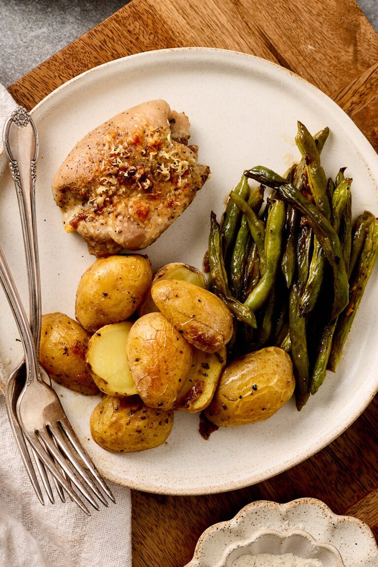 sheet pan ranch chicken thighs served with golden roasted potatoes and fresh green beans on a white plate, perfect for a hearty, home-cooked meal.