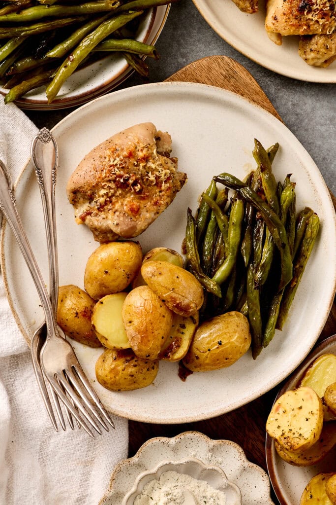Roasted sheet pan ranch chicken thighs with new potatoes and green beans on a white plate, served with lemon wedges, showcasing a hearty and delicious home-cooked meal.