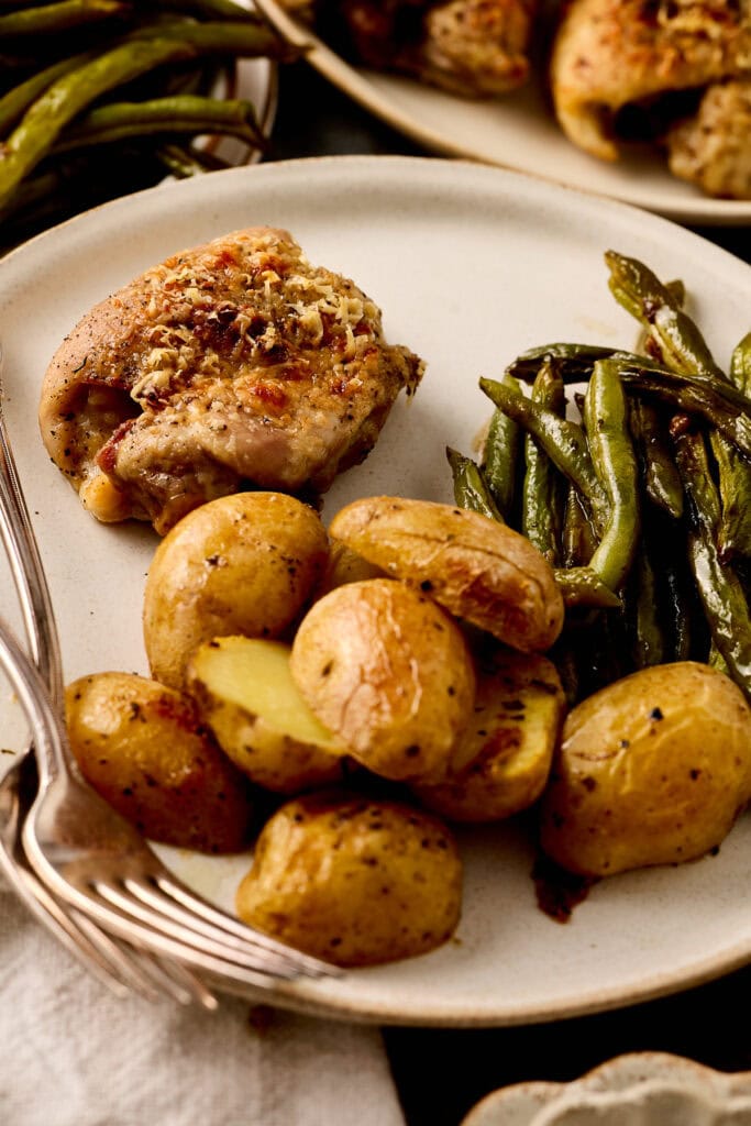 Juicy roasted chicken thigh served with golden baby potatoes and fresh green beans on a white plate, perfect for a hearty, home-cooked meal.