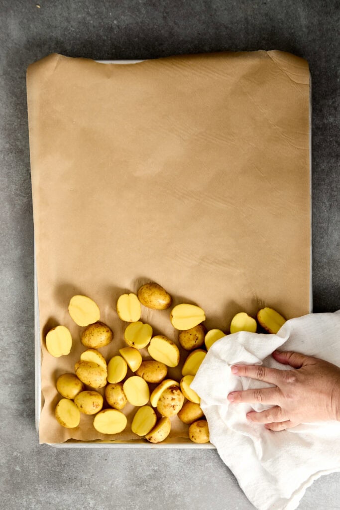 Drying gold potatoes with a white cloth, showcasing golden-yellow potatoes on brown parchment paper.