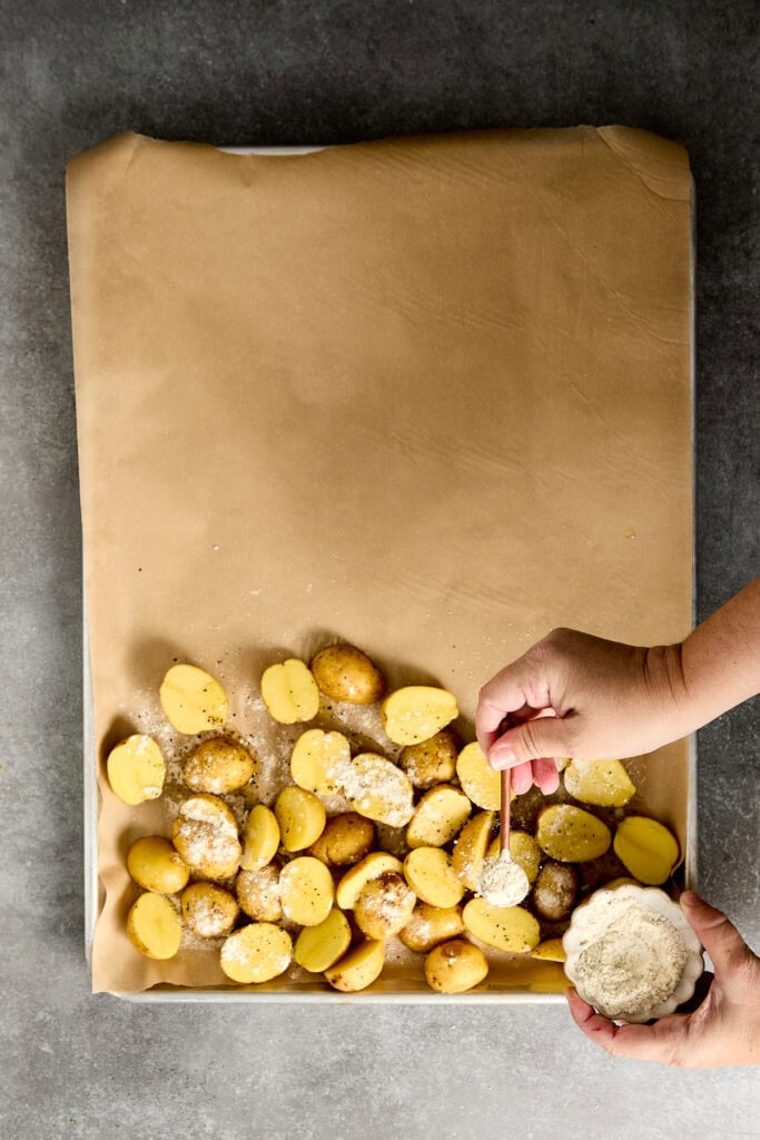 Yellow potato bites being seasoned with salt and herbs on a baking sheet.