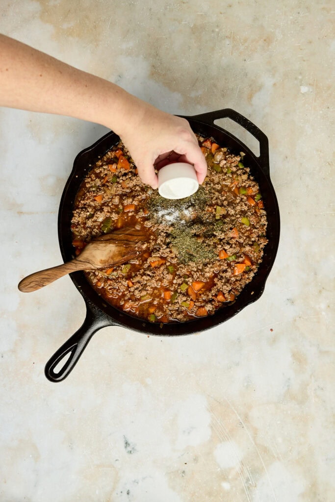Cooking ground beef with vegetables in a cast iron skillet, adding spices for a flavorful meal. Perfect for quick dinners and family-friendly recipes.