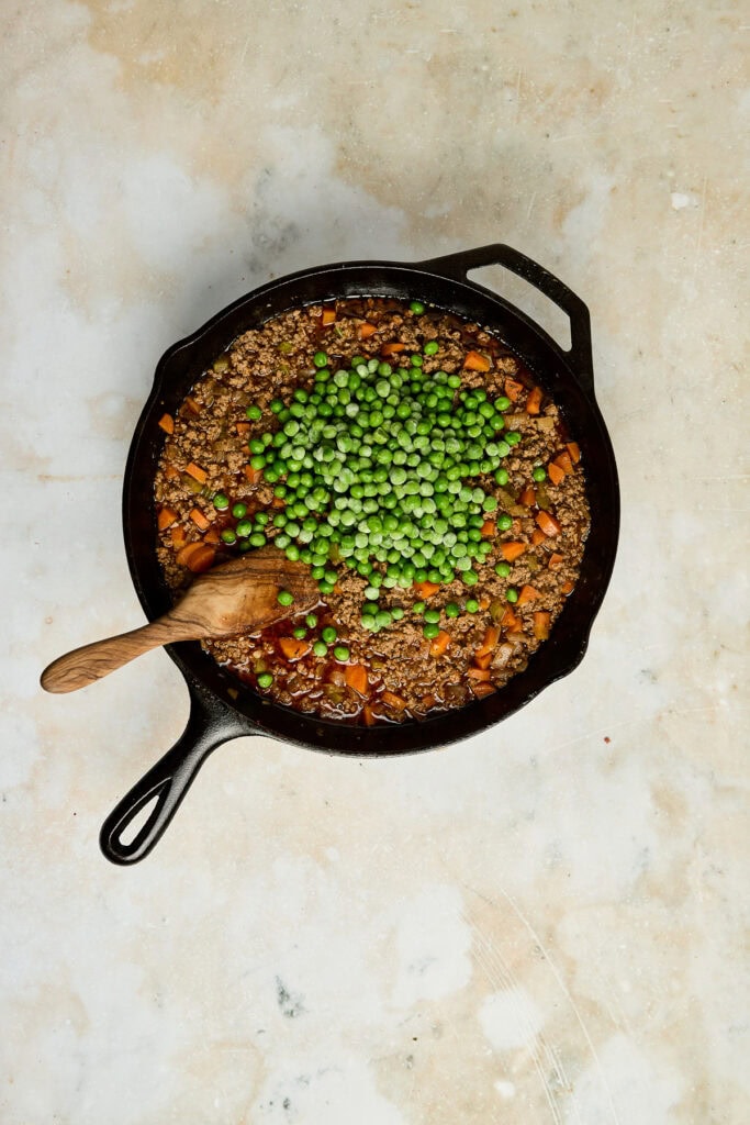 Hearty vegetable beef stew with ground beef, peas, carrots, and potatoes cooked in a cast iron skillet. Perfect comfort food for family dinners and meal prep.
