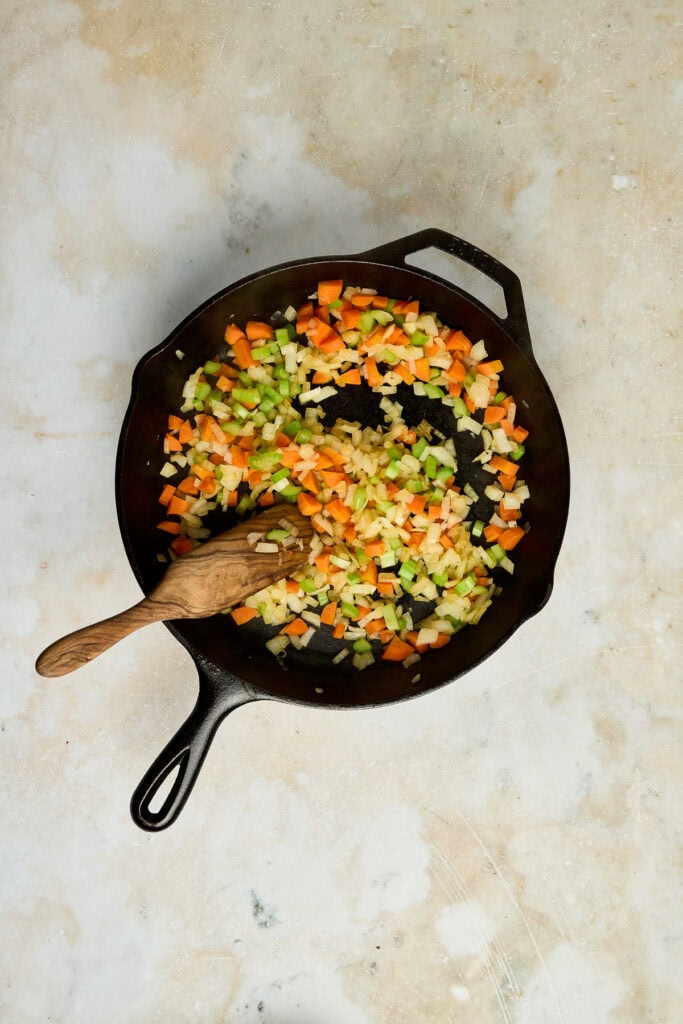 Vegetable stir-fry with chopped carrots, celery, and onions in a black cast iron skillet, ready for cooking. Perfect for healthy recipes, meal prep, or vegetarian dishes.