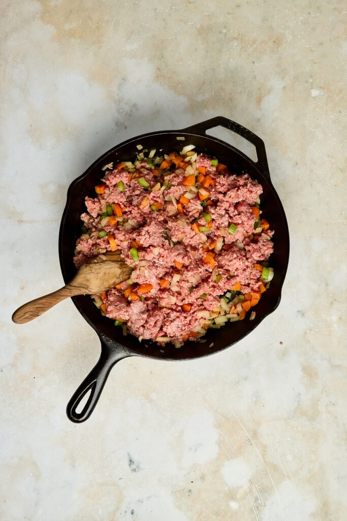 Freshly cooked sweet corn and vegetable hash in a black skillet with diced carrots, celery, and onions, served on a light textured surface.