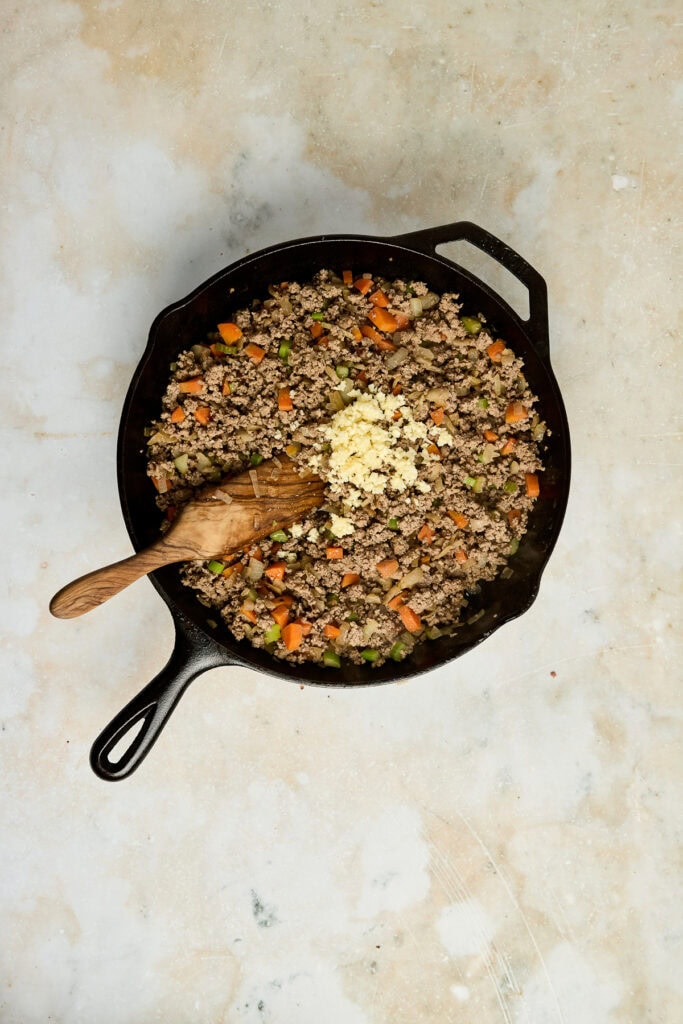Ground beef and vegetable skillet with garlic, cooked in a cast iron skillet, featuring carrots, peas, and minced garlic, perfect for hearty family meals or meal prep.