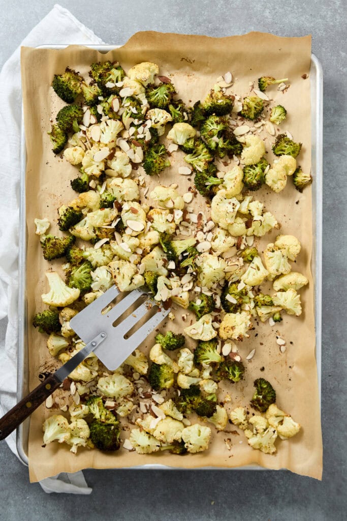 Baked cauliflower florets topped with sliced almonds on parchment paper, ready for serving or further cooking.