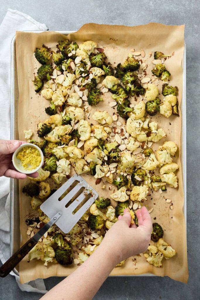 Freshly roasted cauliflower florets on parchment paper, garnished with lemon zest and garlic, ready for seasoning or serving as a healthy side dish.