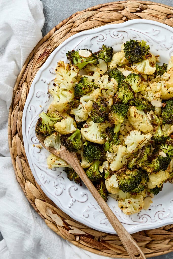 Fresh roasted cauliflower and broccoli florets on a decorative white plate, served as a healthy vegetable side dish, perfect for salads and nutritious meals.