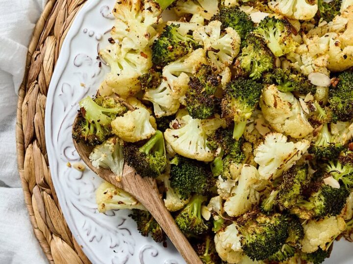 Fresh roasted cauliflower and broccoli florets on a decorative white plate, served as a healthy vegetable side dish, perfect for salads and nutritious meals.