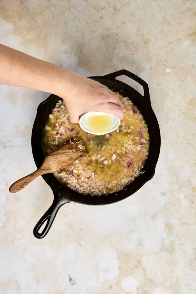Sautéing onions and garlic in a cast iron skillet, with a hand pouring oil over the mixture, ideal for preparing flavorful dishes.