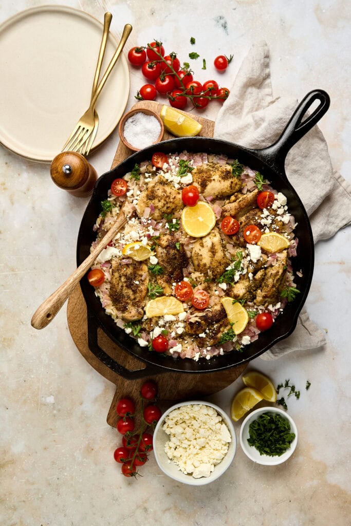 Tasty greek chicken cooked in a skillet with cherry tomatoes, lemon slices, and fresh herbs, served with grated cheese and garnished for a flavorful Italian-inspired meal.